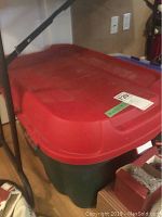 Single large green plastic tote bin with red lid viewed from above, showing textured lid with handle.