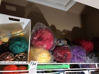 Yarn skeins in a white plastic basket and some loose yarn skeins in assorted colors including greens, yellows, reds, purples, and browns