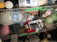 Shelf with various yarn skeins including white, pink, gray, blue and red along with packaging and partially finished knitting project.