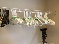 Photo showing wire rack with bundles of white plastic hangers, some green and brown hangers, and a black Conair garment steamer standing on the floor beneath the rack.