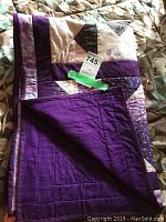 Folded view of the quilt showing patchwork front and solid purple backing