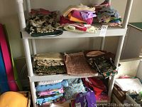 Full view of three white plastic shelves with various folded and rolled fabric pieces in different patterns and colors