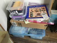 Overall view of stacked plastic storage boxes with quilting supplies including fabrics and a quilting book on top.