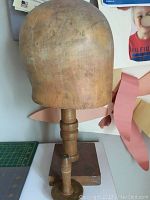 Full view of the wooden hat block head on stand showing the shape, texture, and base.