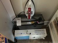 Photo of swing arm lamp in original box, Proctor Silex steam iron on top, and paper shredder beneath.