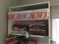 Top shelf with three fabric storage baskets in pastel colors, and two lower shelves with stacks of folded quilting fabric pieces in multiple patterns and colors.