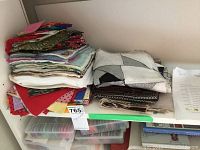 Folded stacks of assorted fabrics in different colors and textures on a shelf, showing varied textile types and some sewing projects in progress.