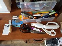 Overview of assorted scissors, rotary cutters, blades and storage box on wooden surface