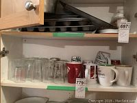Cabinet shelf showing 8 Tim Horton mugs including 7 large and 1 smaller, 2 small mason jars, and some drinking glasses.