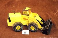 Photo of vintage metal Tonka loader toy showing yellow paint with chipping and black front bucket on brown carpet background with lot number card.
