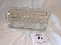 Glass butter dish with lid placed on surface, showcasing textured glass pattern and rectangular shape.