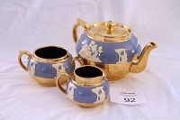 Complete tea set including teapot with lid, creamer, and sugar bowl with blue and gold colors, white relief design.