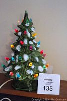 Front angled view of green ceramic Christmas tree lit with multi-colored bulbs and white snow-like accents, standing about 11 inches tall.