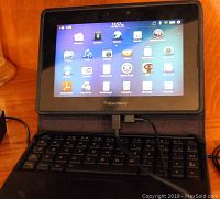 Front view of the BlackBerry PlayBook tablet showing the home screen with multiple app icons, attached to the mini keyboard.