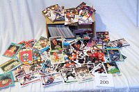 Wide view of large pile of assorted hockey trading cards spread on a surface with some still in partial stacks and a box visible behind.