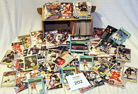 Photo showing a large assortment of hockey trading cards spread out on a surface with a cardboard box holding more cards behind.