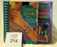 Front cover of the Klutz Paper Beads craft book with an attached plastic tray containing multiple decorated paper strips, glass beads, thread, glaze, and crafting tools.