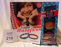 Front cover of the Ribbon Bangles kit by Klutz showing the book and ribbon storage compartment with colorful bracelets on the cover model's wrists.