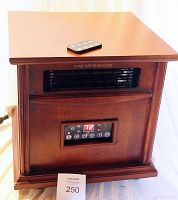 Full view of wooden cabinet style electric heater with remote control on top.