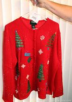 Front view of red holiday sweater with green Christmas tree and festive decorations including ribbons, bows, beads, snowflakes and gifts.