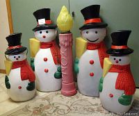 Photo showing four snowman figures and one tall candle decoration arranged on carpeted floor, details on size and design visible