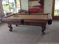 Overview of solid wood pool table in room, showing carved legs and leather drop pockets