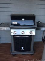 Front view of black and stainless steel Weber Spirit gas grill with three control knobs, temperature gauge, side shelves, and Wheeler base.