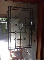 Front view of the leaded glass window pane hanging indoors with natural light showing frosted textured glass and lead framework.