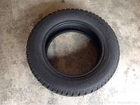Top-down photo of a single black Les Schwab Winter Pike snow tire on concrete floor, showing tire tread pattern and sidewall.