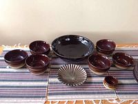 Top-down view of large dark brown ceramic bowl and array of smaller soup bowls in brown and beige glazes surrounding decorative small plate.