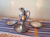 Overview of sterling pitcher and three silver-plated trays on striped cloth