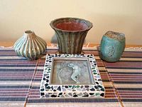 Three ceramic pots and framed watercolor painting arranged on striped placemats, showing overall contents of lot