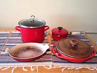 Front view of four red French cookware items on table with cloth covering