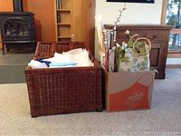 Photo showing a large open rattan chest with tissue paper inside next to a box filled with gift bags and wooden decorative sticks.