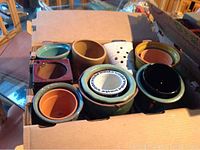 Box containing various small plant pots made of ceramic and glazed clay, showing assorted colors and shapes.