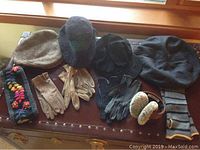 Photo showing 4 gloves, 4 hats, warm knit headband with pom-poms, and fur-lined earmuffs with striped band arranged on a surface.