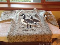 Grey flecked knit crewneck sweater with bird motif laid flat on white surface.