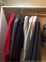 Six robes hanging on closet rod in various colors and fabrics including fleece and terry cloth.