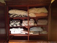 Full view of linens including linens stacked on shelves inside wooden wardrobe.