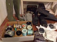 Photo showing two pairs of wading boots in green and black, knit gloves, and a box containing fishing reels and line spools.