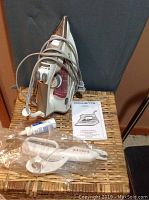 Rowenta steam iron on wicker hamper lid with spray bottle, manual, and Singer electric scissors