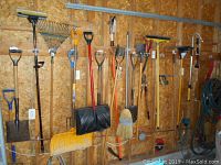 Wide view of the wall holding various garden tools including rakes, shovels, brooms, and trimmers.