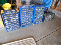 Wide view showing four blue metal storage units with many small clear plastic drawers containing assorted hardware items.