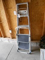 Five foot aluminum step ladder leaning against unfinished wood wall beside two-step stool folded.