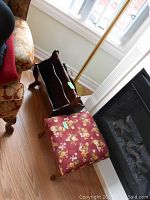 Floor lamp next to window with wood magazine rack and floral fabric foot stool visible on the wooden floor.
