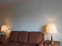 Two brass-toned tri light table lamps placed on either side of a brown sofa, both lamps turned on emitting warm light.