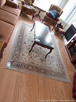 Rectangular beige, brown, and cream floral patterned area rug under a wooden coffee table with glass top in living room setting.
