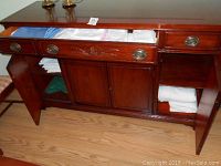 Opened wooden cabinet showing folded table linens including several white cloths where napkins and tablecloths are stored