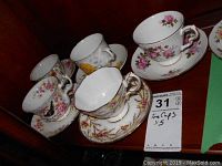 Five sets of Royal Albert tea cups in various floral patterns with matching saucers displayed on a shelf.