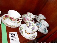 Five sets of tea cups and saucers on a wooden shelf, each with floral patterns and gold trim.